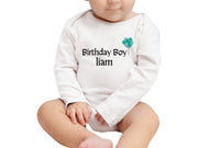 a baby sitting on the ground wearing a birthday boy shirt