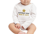 a baby sitting on the ground wearing a birthday star onesuit