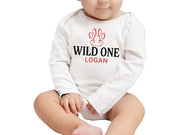 a baby sitting on the ground wearing a long sleeved bodysuit